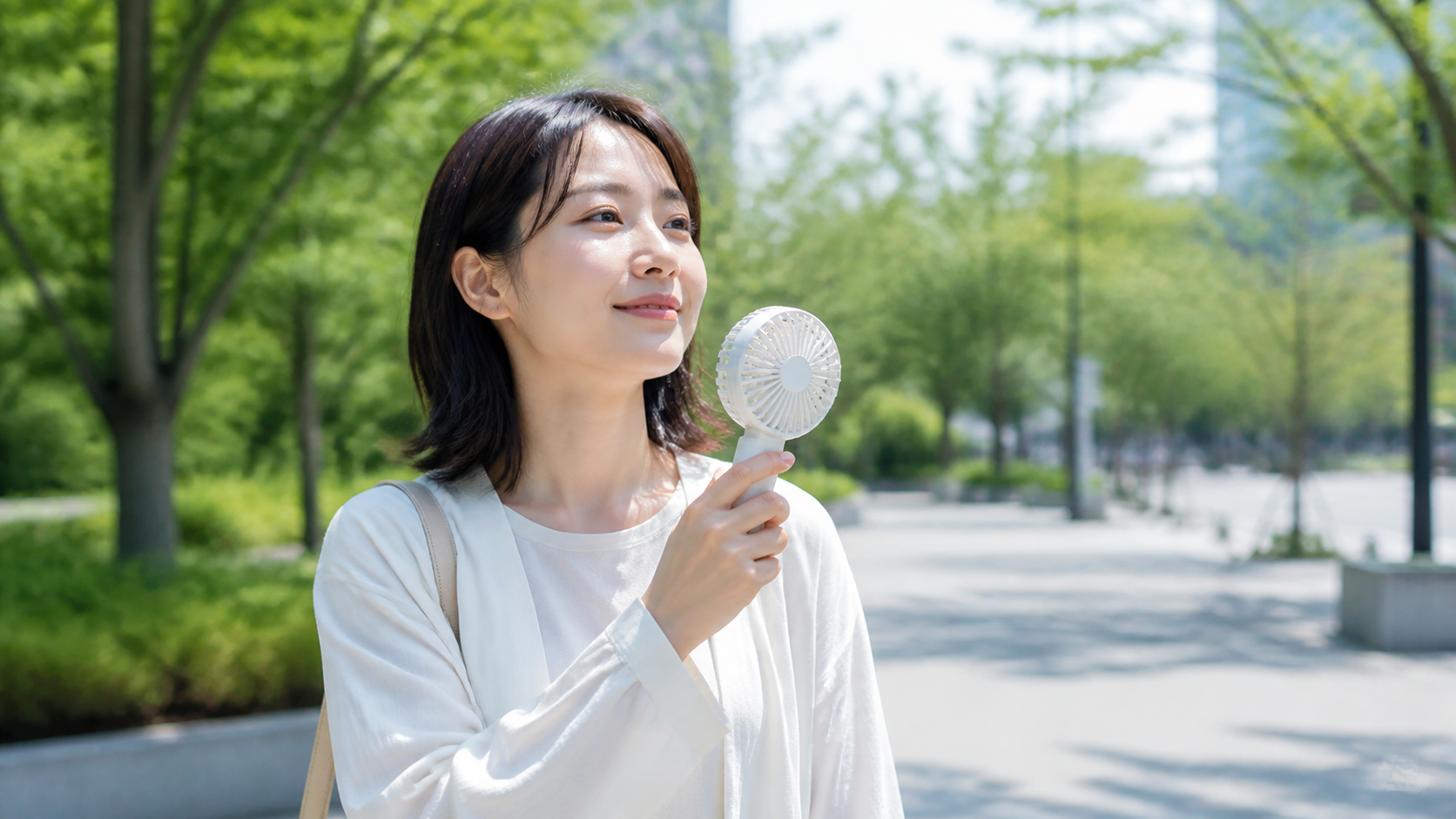 夏の屋外でハンディファンを使うイメージ